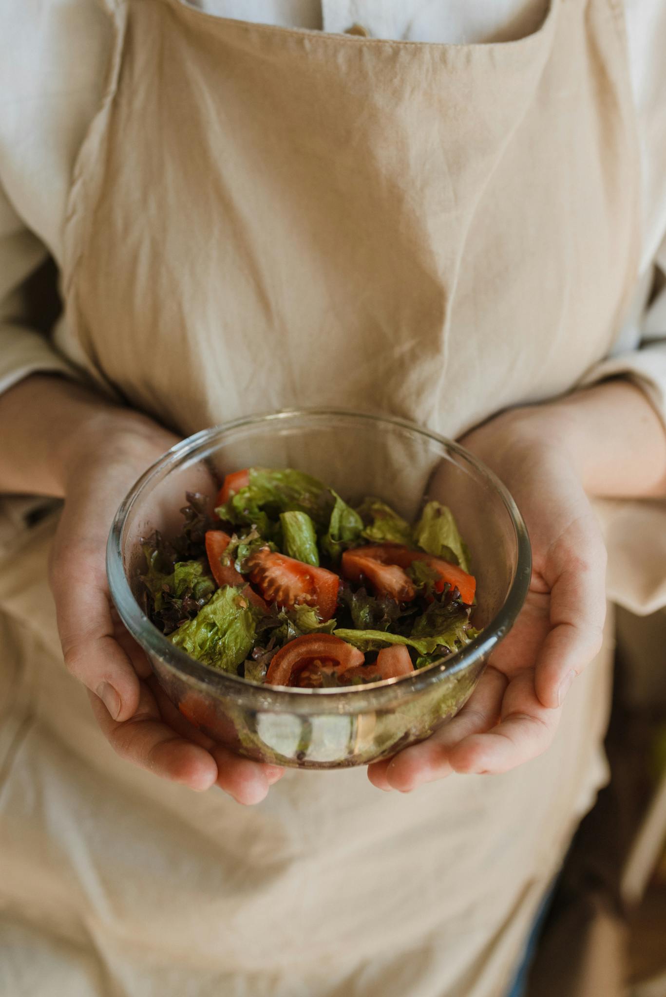 Close-up of a healthy homemade vegetable salad with lettuce and tomatoes held by a person in an apron.